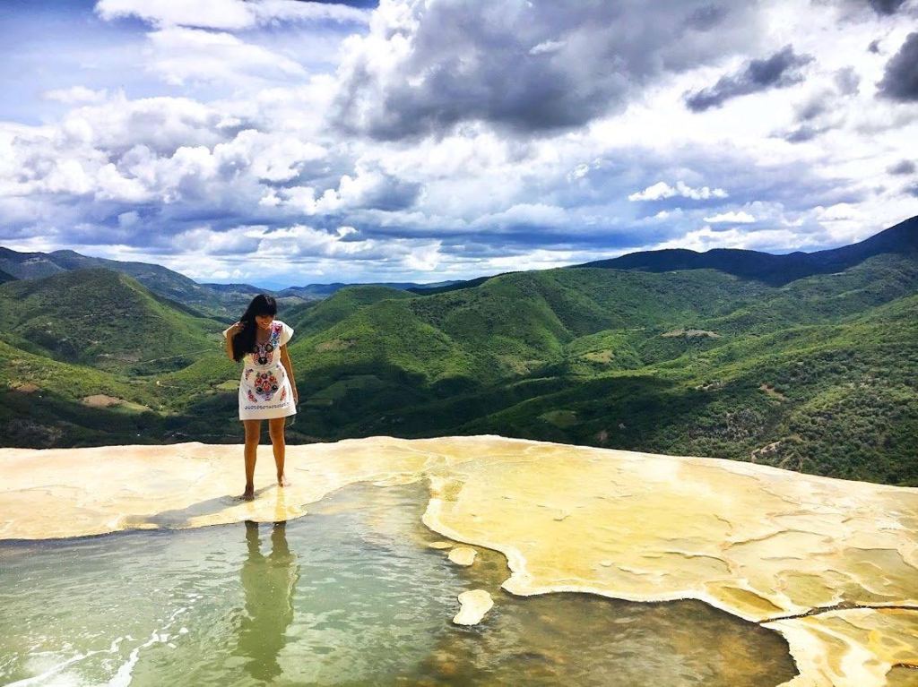 Girl standing on the edge of a cliff in a natural spring water pool and mountain range behind her in Oaxaca Mexico Hierve El Agua