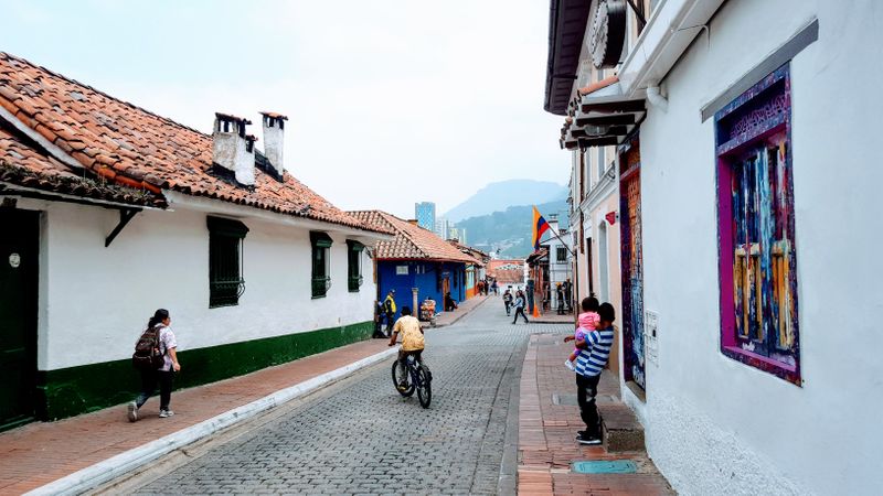 Streets in Bogota with school girl, boy riding a bike, mountain backdrop and white houses.