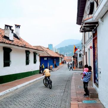 Streets in Bogota with school girl, boy riding a bike, mountain backdrop and white houses.